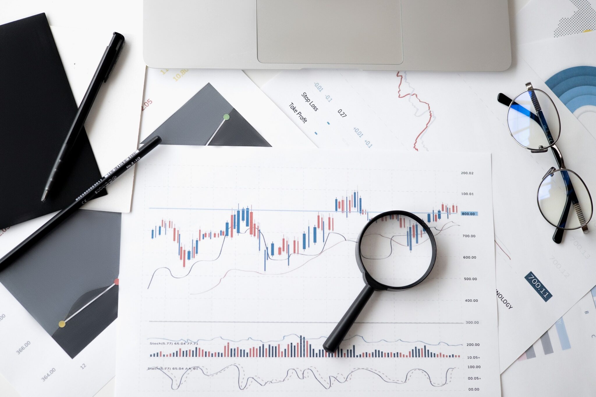 graph of stock prices with magnifying glass and readers on a desk